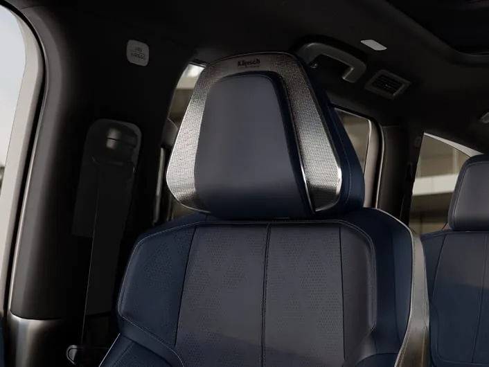 Close-up of a deep navy quilted leather front seat in the 2027 INFINITI QX80 SPORT, with a brushed-metal Klipsch speaker surround built into the headrest.