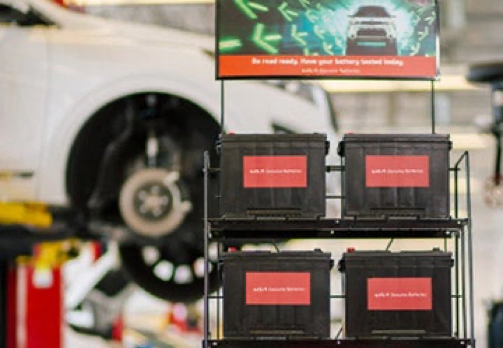 Display rack of four Kia Genuine Batteries in a service bay, beneath a banner reading "Be road ready. Have your battery tested today."