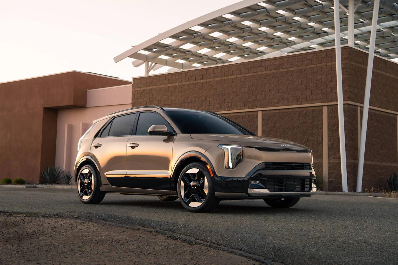 Bronze 2027 Kia Niro parked outside a modern desert building with a solar-panel awning overhead.