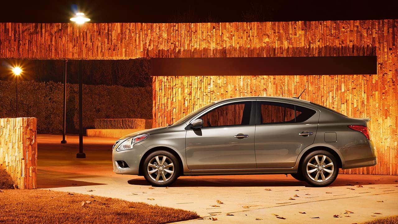 Gray 2017 Nissan Versa sedan parked in front of a lit wooden wall at night