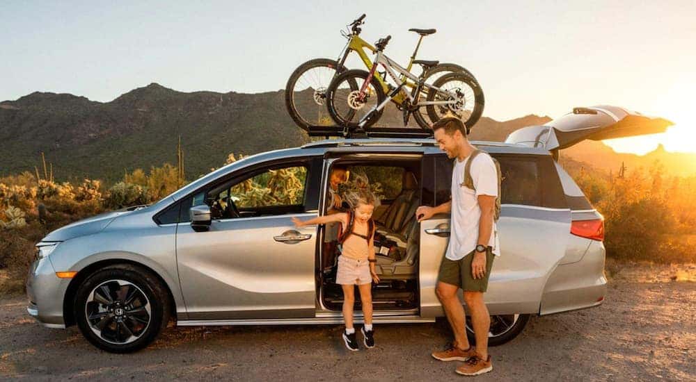 A silver 2021 Honda Odyssey is shown in profile with a family going bike riding.