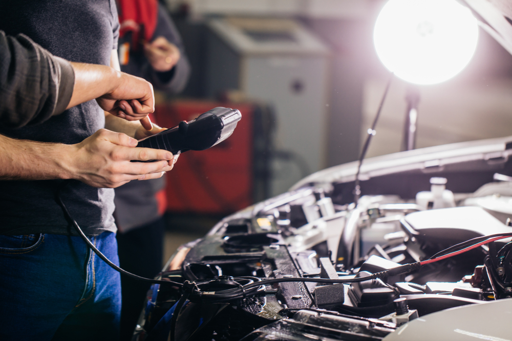 Multimeter hooked up into the engine of a car , the hood is open and two people are working the multimeter