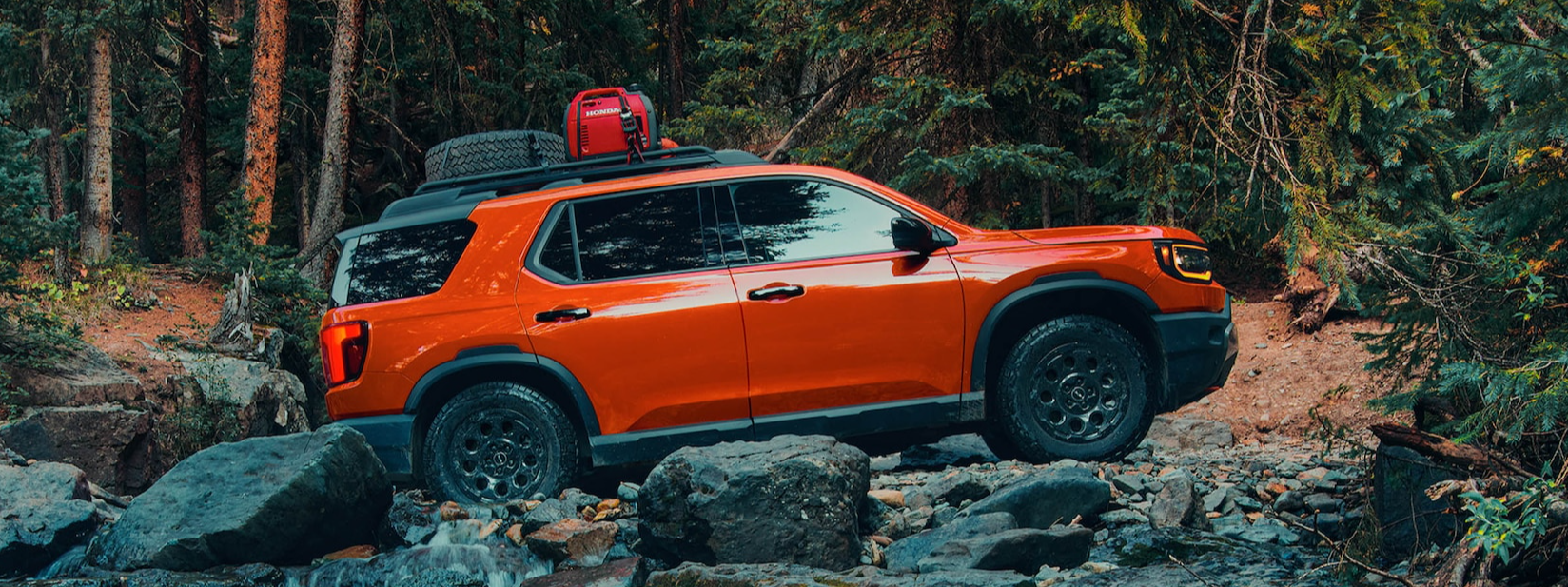 The new, red 2026 Honda Passport is shown from the side driving off-road over jagged rocks through the forest.