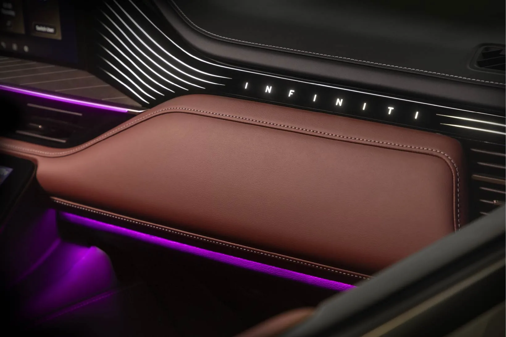 Close-up of the 2027 INFINITI QX80 passenger dashboard with a backlit INFINITI logo, burgundy leather, and purple ambient light in the footwell.