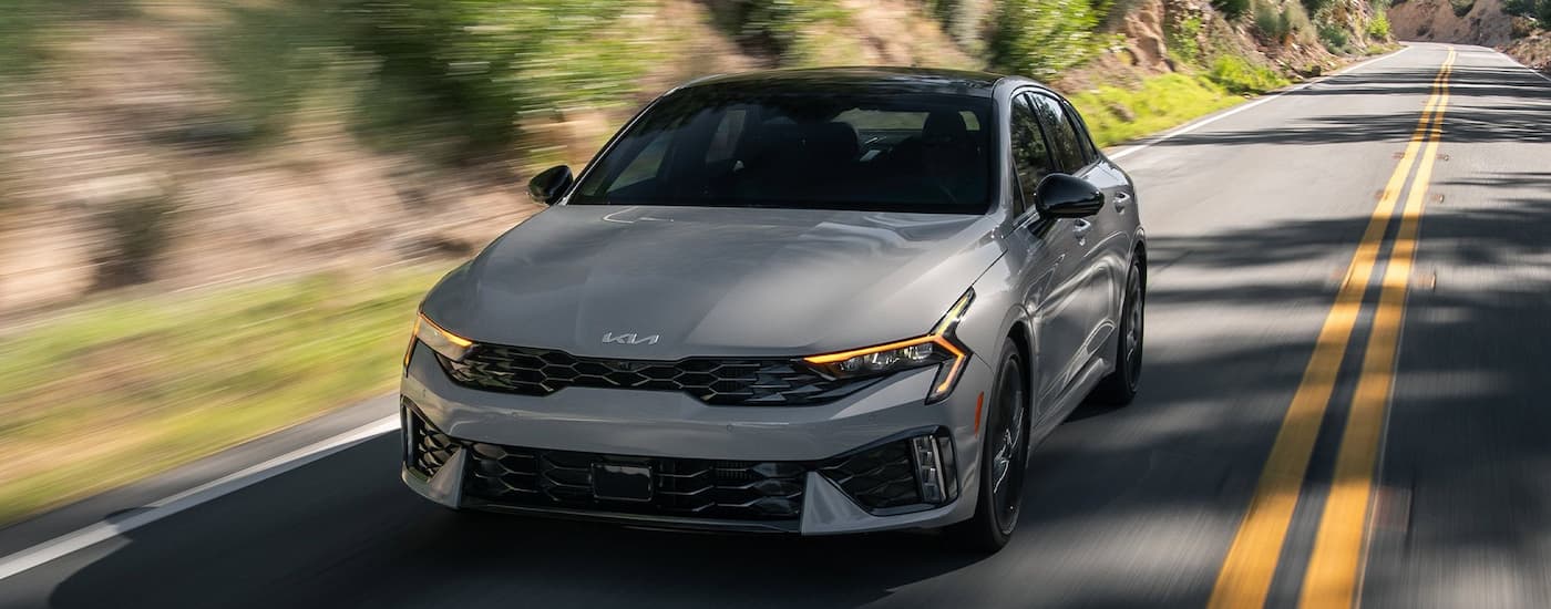 Grey 2026 Kia K5 driving down a road.