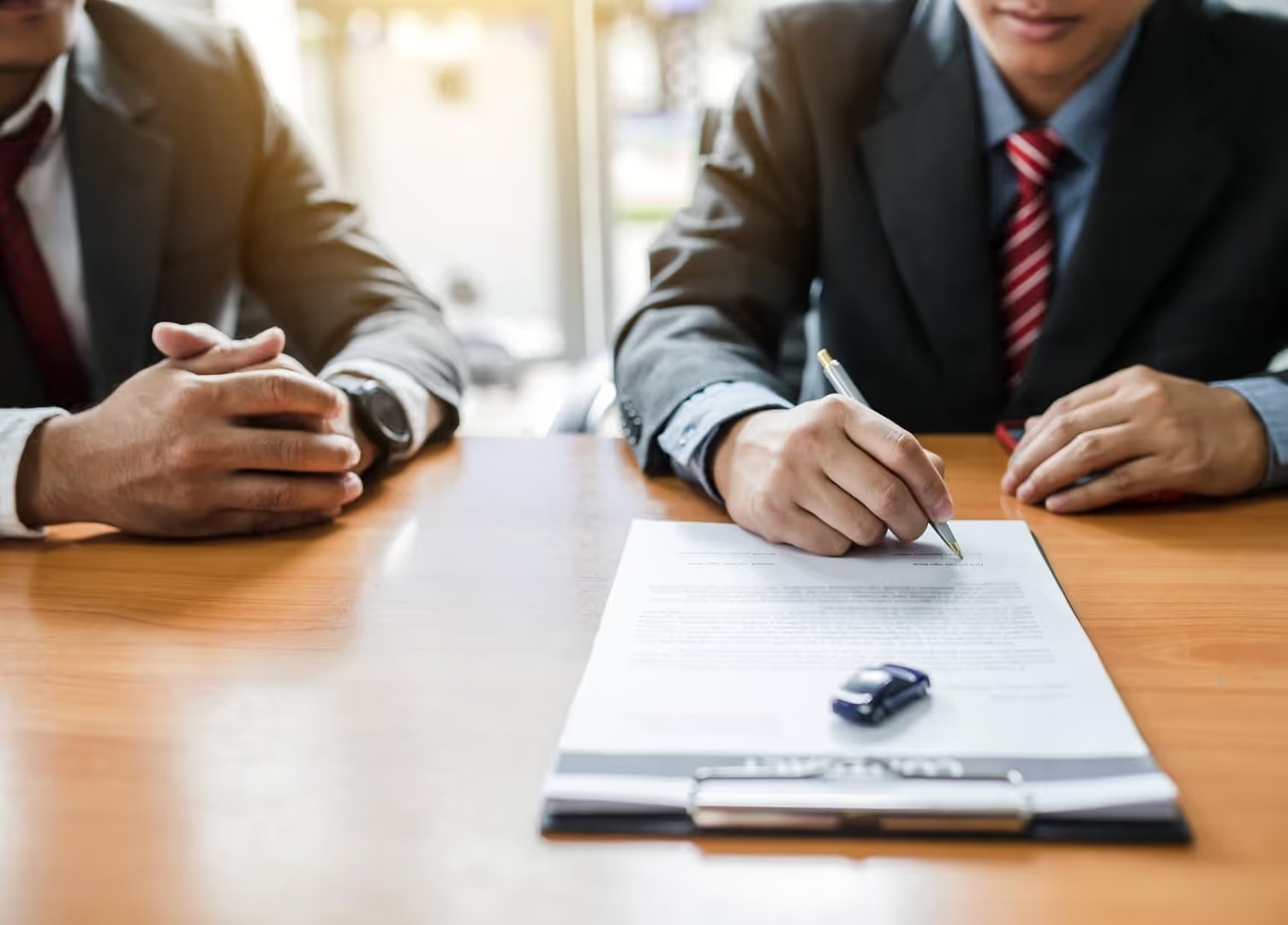 Two people at a desk signing vehicle paperwork with a toy car on the contract