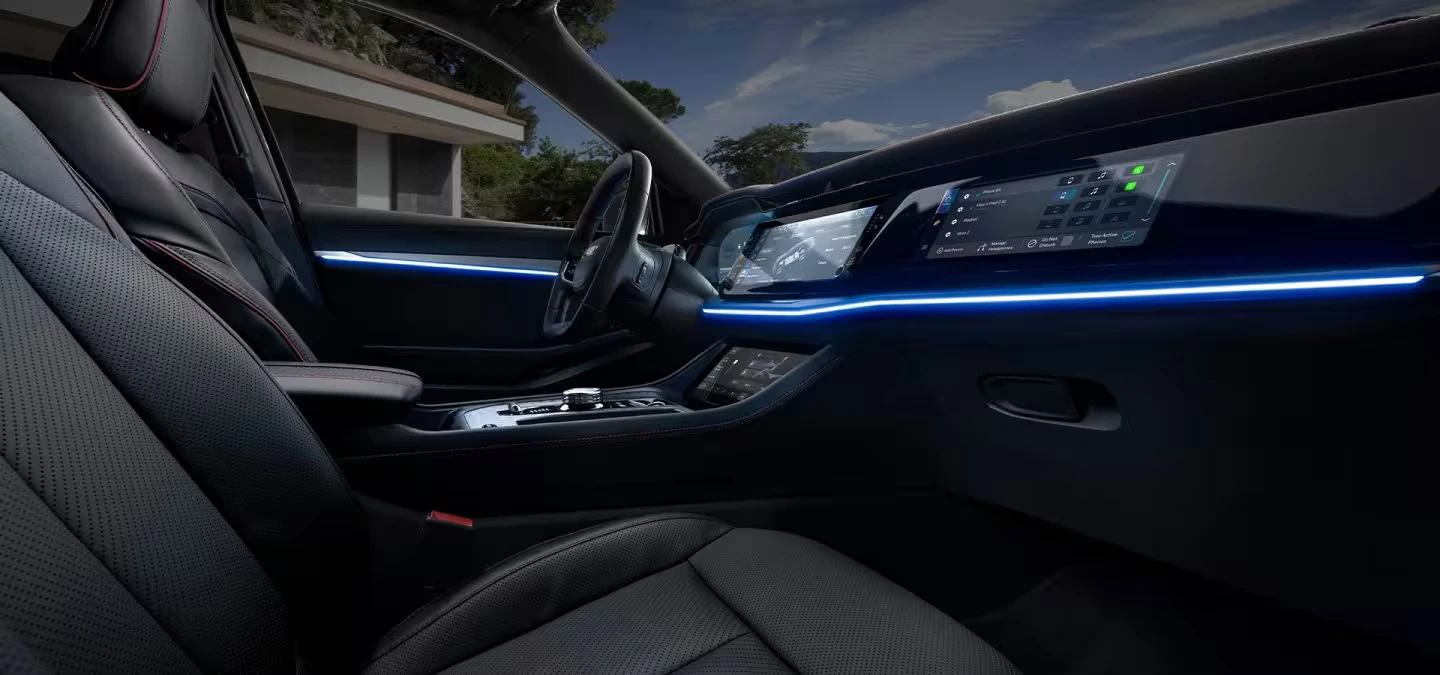 Front interior of the Jeep Wagoneer S with black perforated seats, wide dashboard screens, a rotary gear selector, a lower touchscreen and glowing blue ambient lighting along the dash and door
