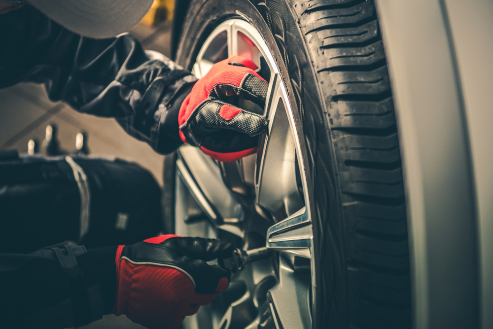 Mechanic with Red and Black Gloves on changing tire on car