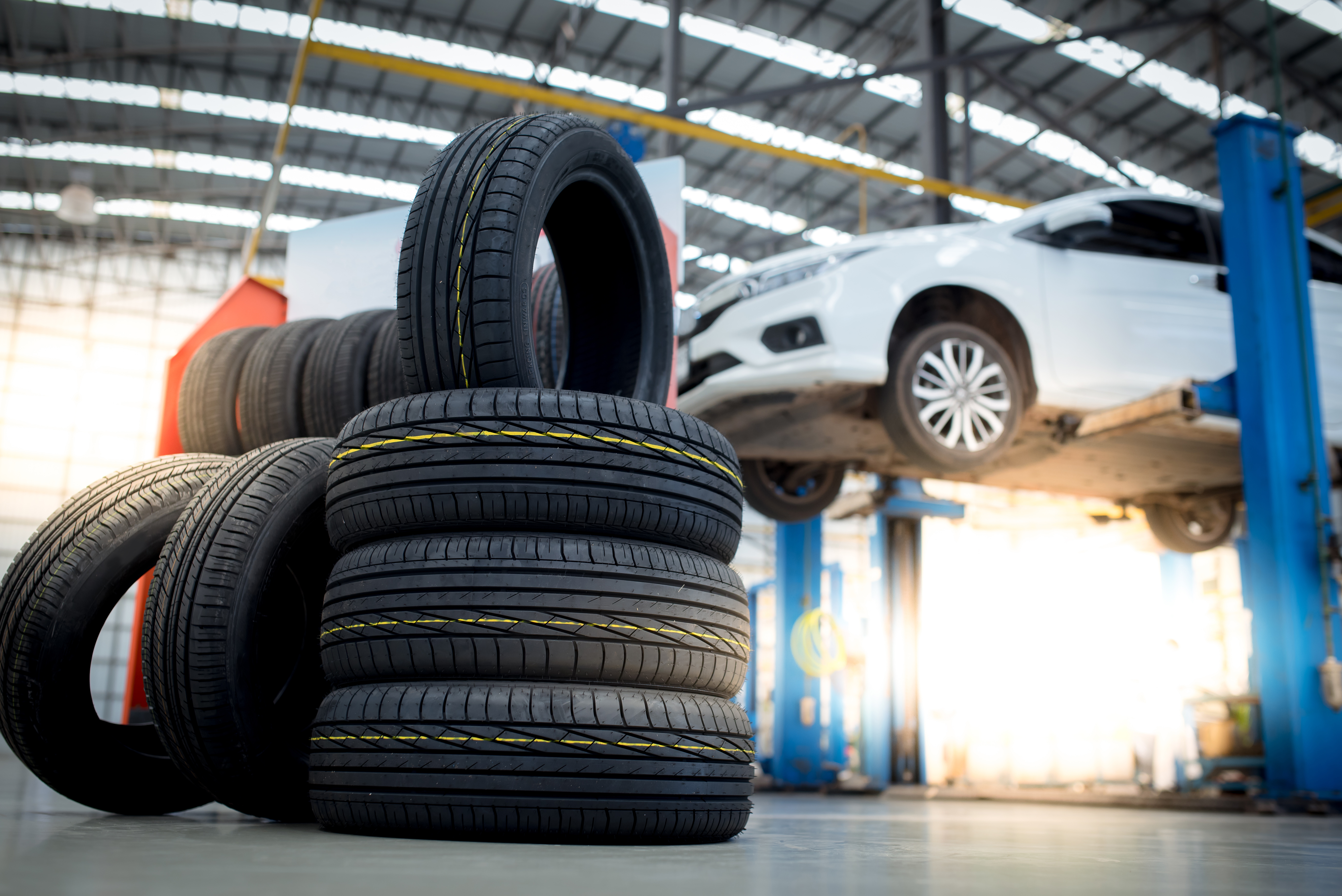 in focus: stack of tires in a service center; in background: white car on a mechanic lift in the service center