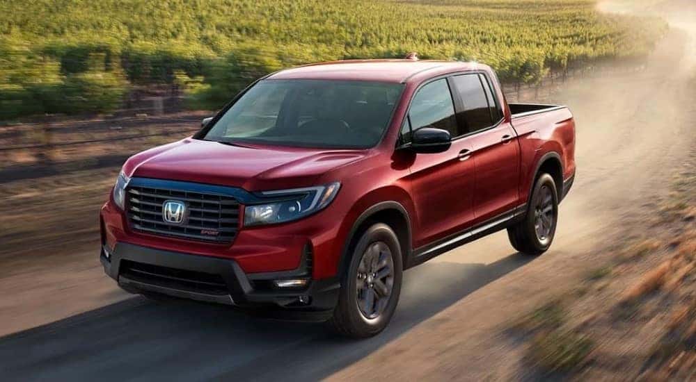 A red 2024 Honda Ridgeline Sport driving on a dirt road.