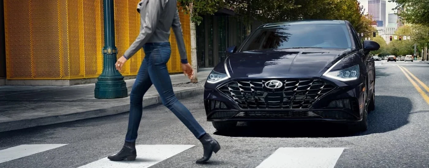 Black 2023 Hyundai Sonata stopped at a crosswalk with a woman walking across