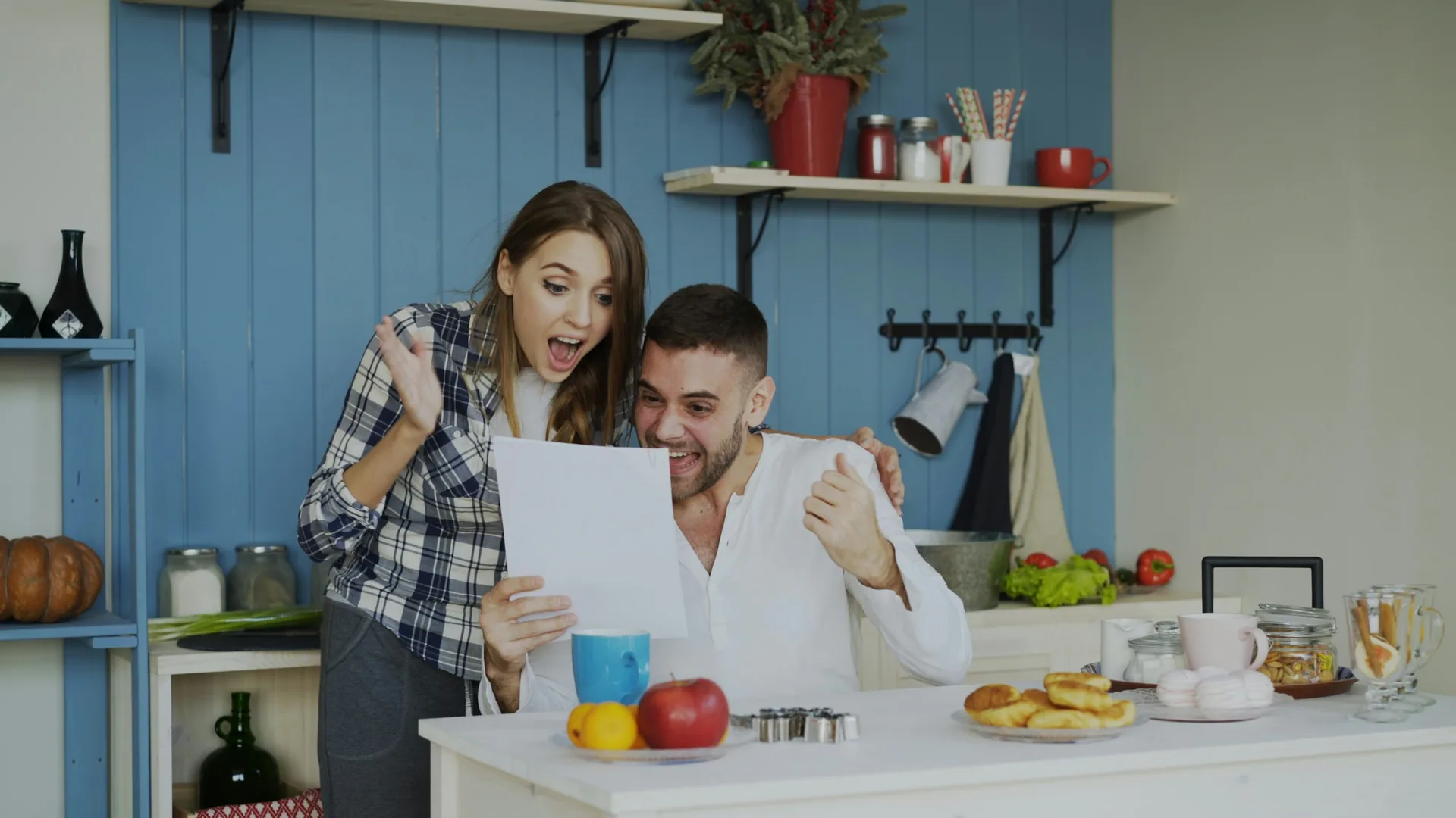 Man and woman in a home kitchen smiling and reacting excitedly while looking at a piece of paper together