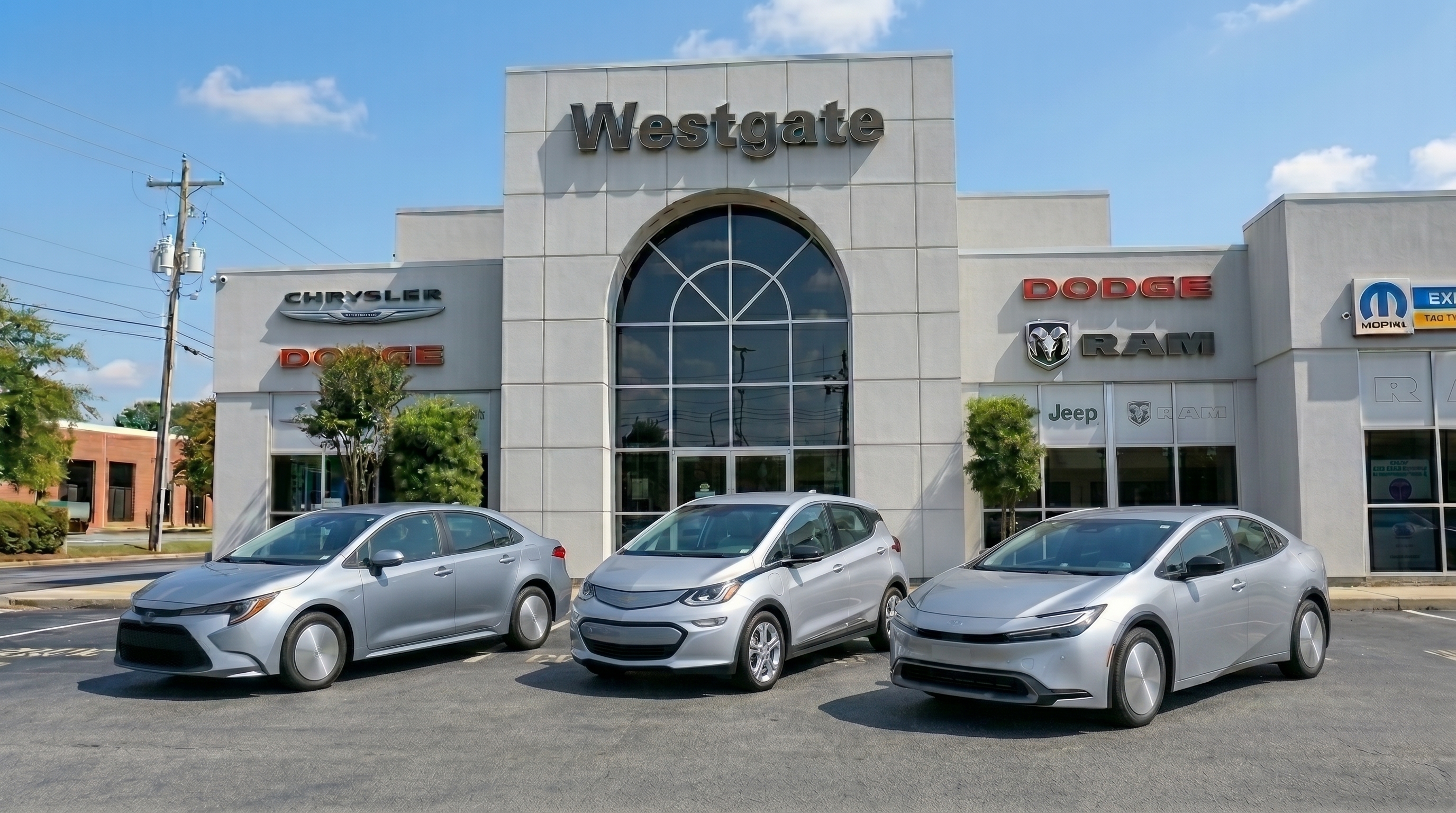 A lineup of fuel-efficient pre-owned vehicles, including a silver Toyota Corolla, a Chevy Bolt EV, and a Toyota Prius, parked in front of the Westgate Chrysler Jeep Dodge Ram dealership showroom building in Raleigh.