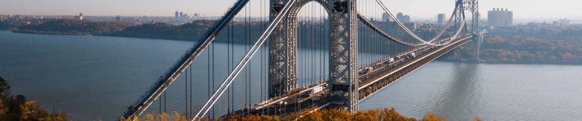 Aerial view of a large suspension bridge spanning a river with a city skyline in the background.