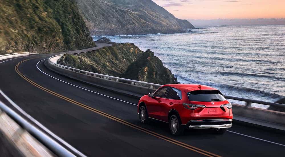 Rear view of a red 2025 Honda HR-V EX-L driving by the coast.