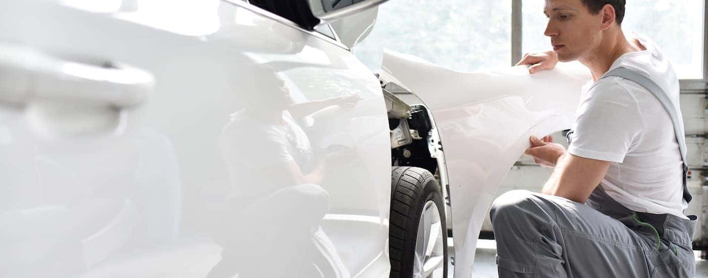 A mechanic is shown putting a fender on a white vehicle.
