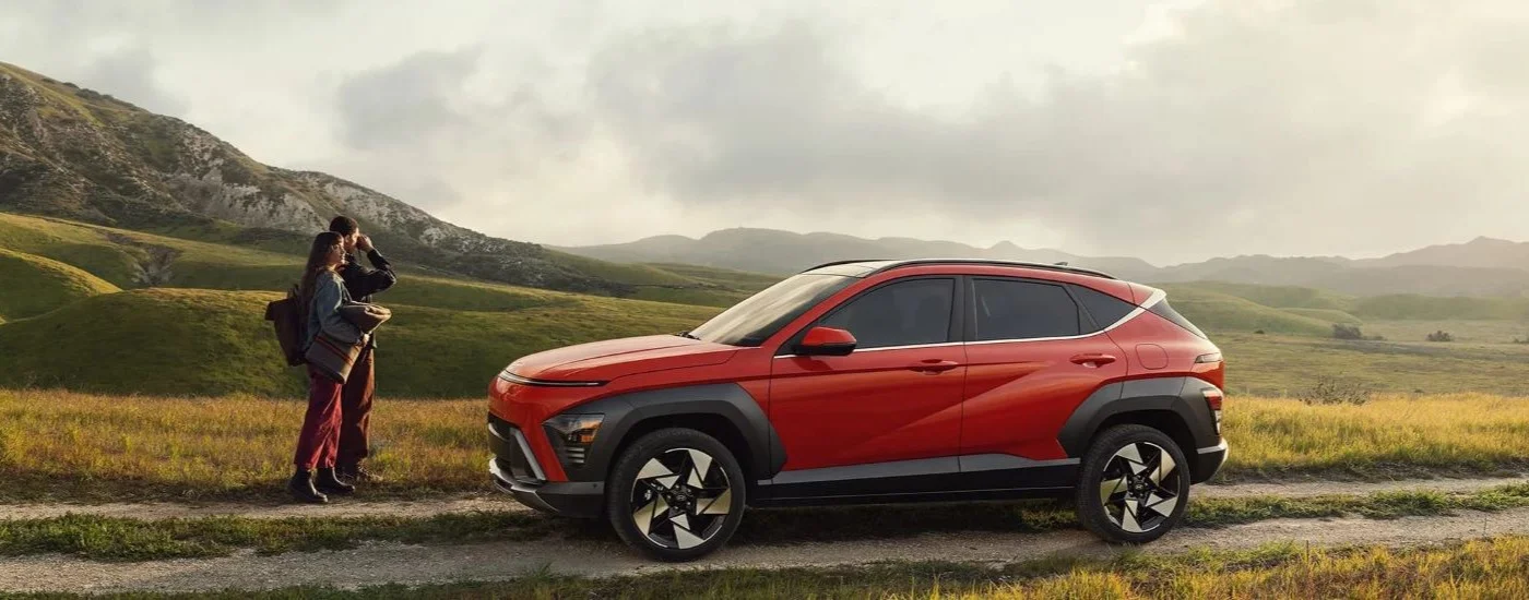 Red 2024 Hyundai Kona parked off-road with a couple standing in front of it