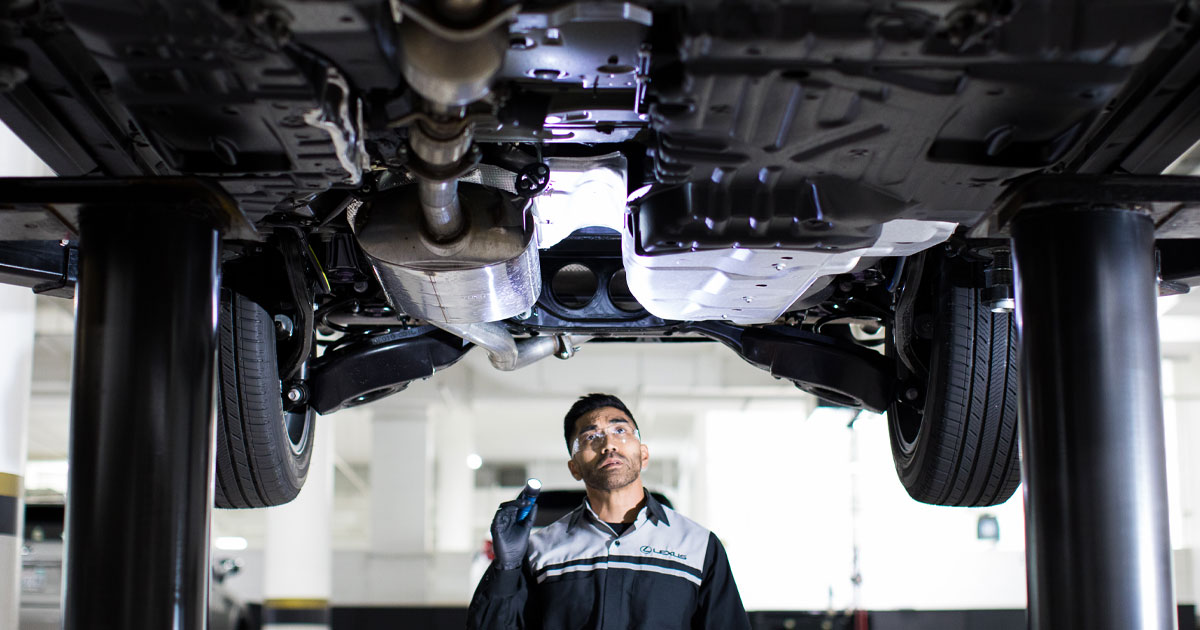 A service technician inspecting the underside of a vehicle on a lift in the service center.