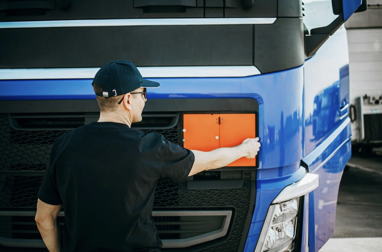 A truck driver in a cap inspecting the front of a large blue semi-truck during a pre-trip check.
