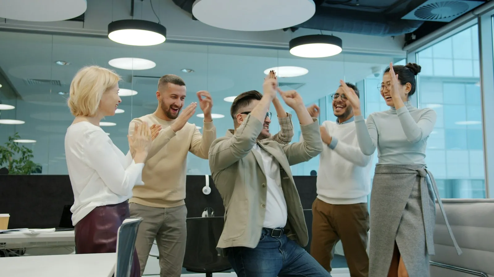 A team of coworkers high-fiving and celebrating together in a modern office.