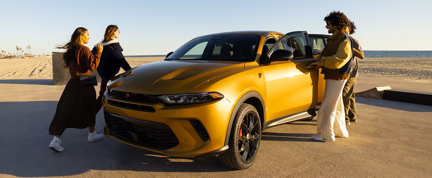 Group of people standing near a 2024 Dodge Hornet parked by the beach, highlighting its sporty exterior