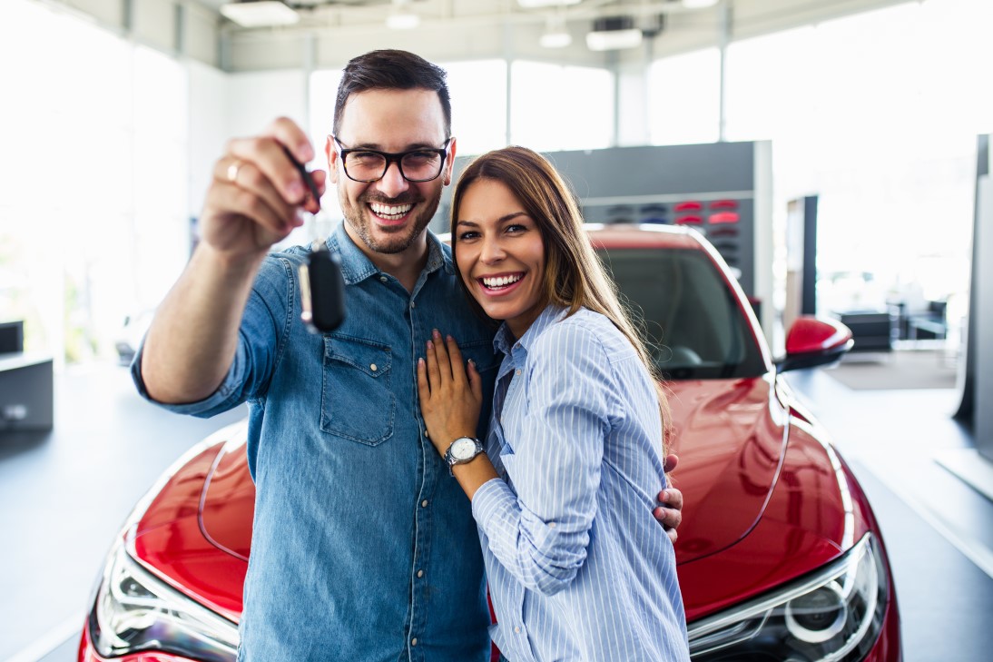 couple smiling and holding up a car key, standing in front of car