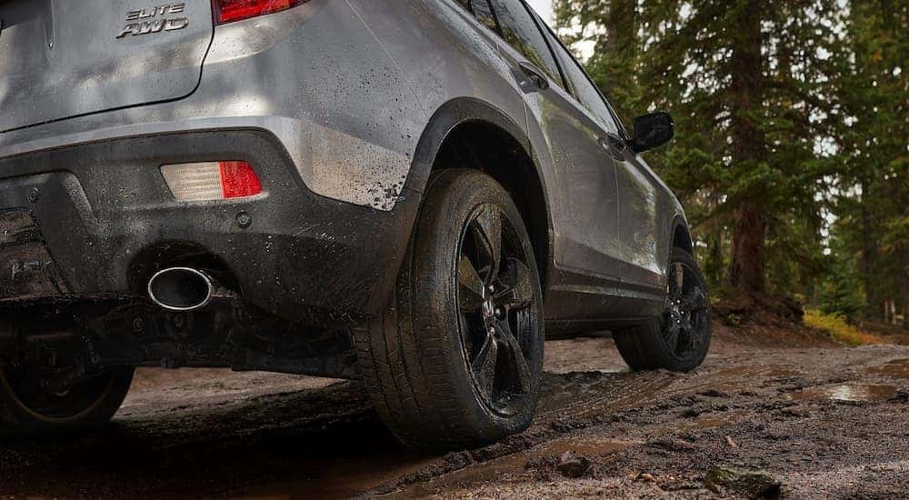 The rear tire and bumper of a silver 2022 Honda Passport Elite AWD is shown while driving on a dirt road