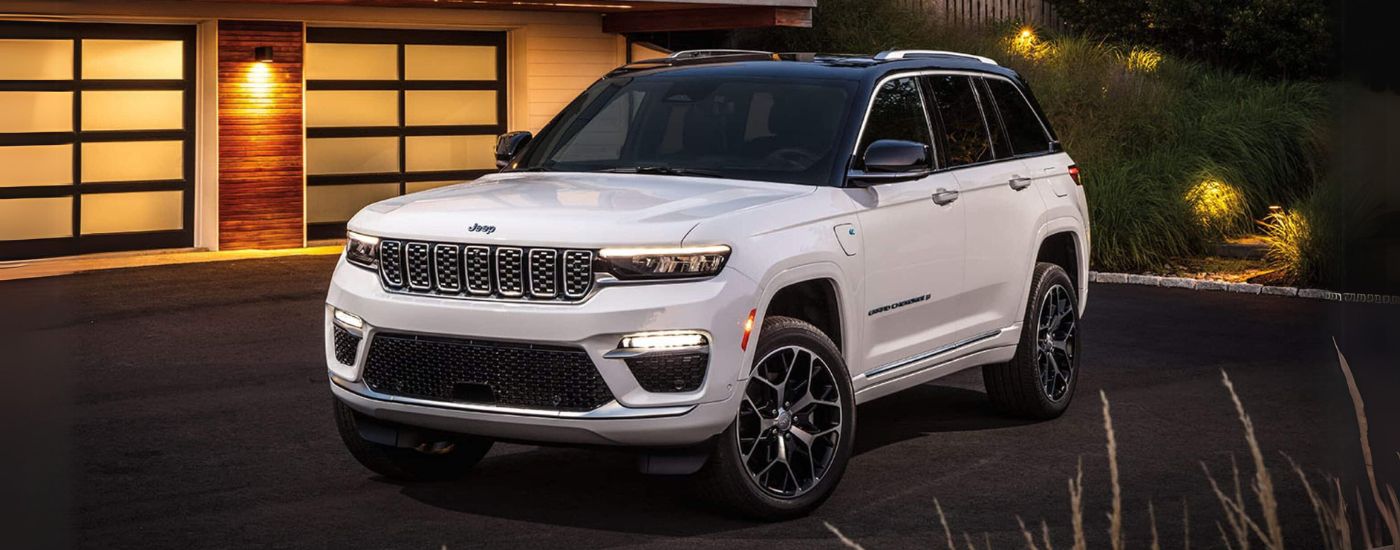 A white 2024 Jeep Grand Cherokee Summit Reserve 4xe is parked in a driveway.