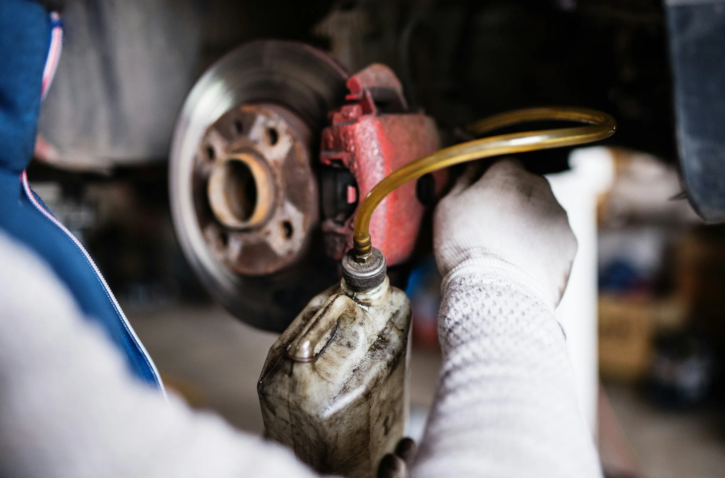 Gloved technician's hand applying fluid to a red brake caliper during a brake service. Brake Fluid Service in Kansas City, KS