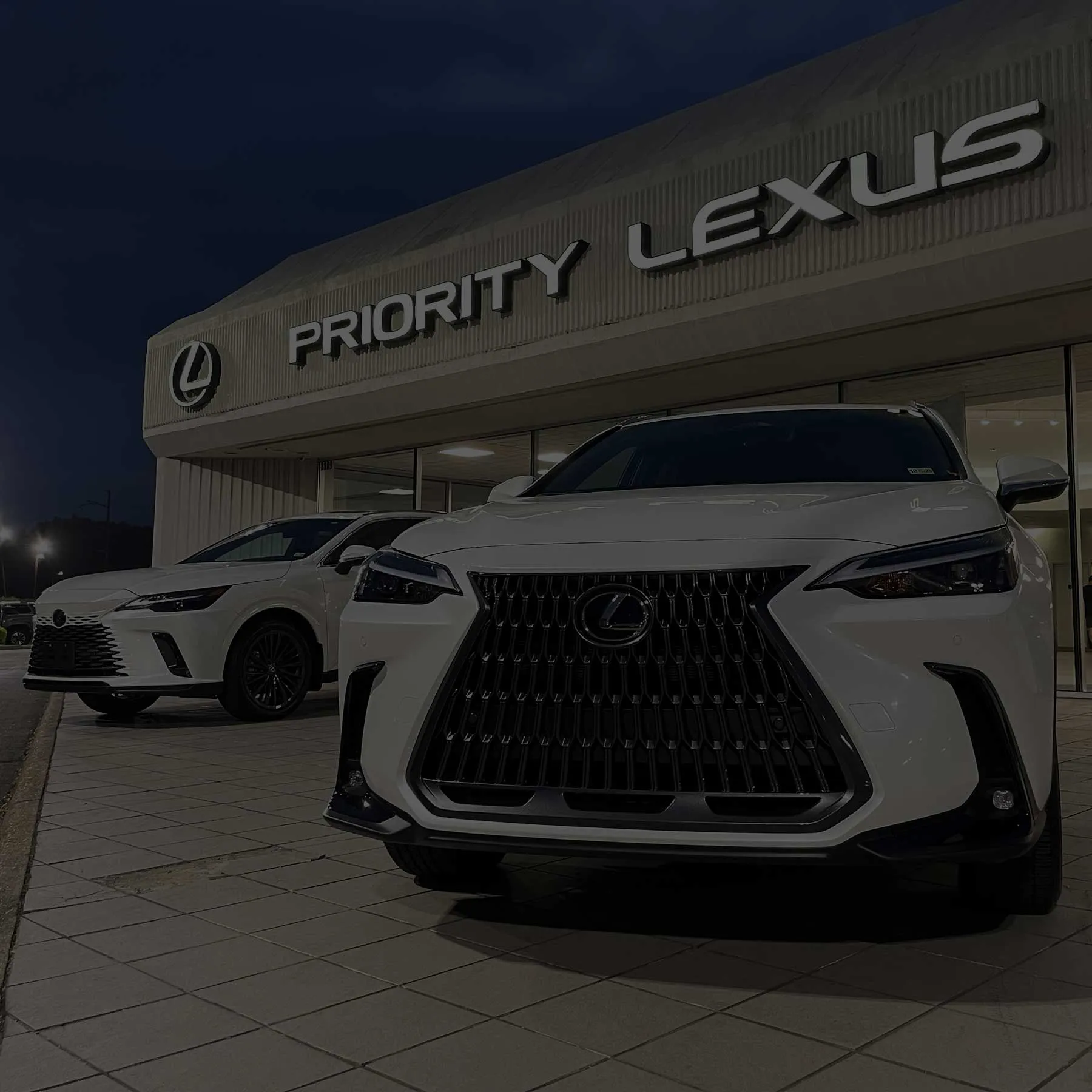 [[dealerName]] dealership storefront at night with two white Lexus vehicles parked out front
