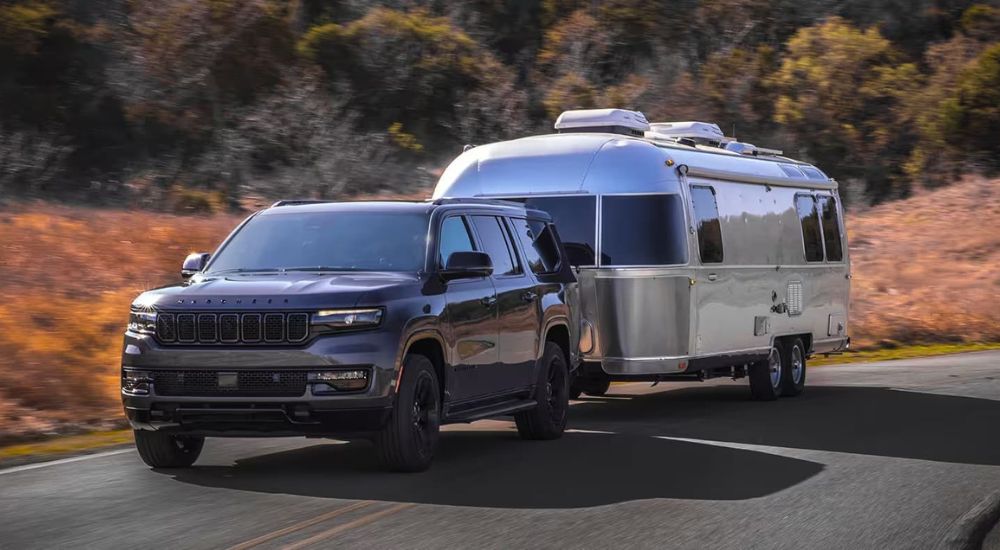 A grey 2022 Jeep Wagoneer is shown towing a trailer to a used Jeep dealer.