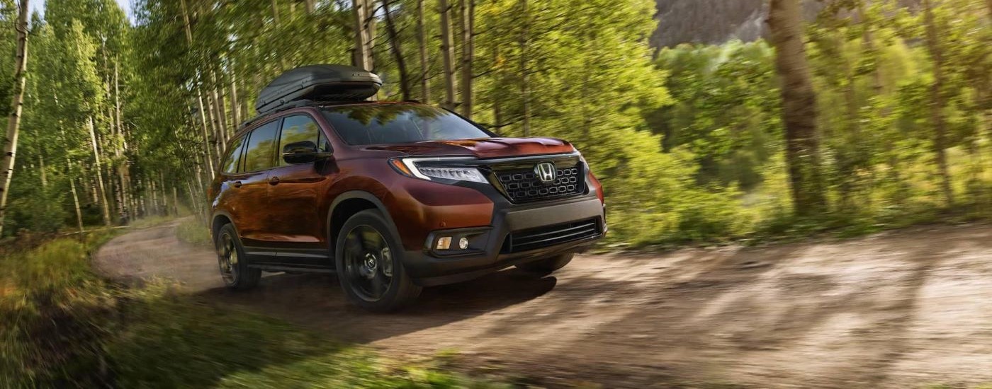 A red 2020 Honda Passport is driving on a dirt road near Rochester, NY.
