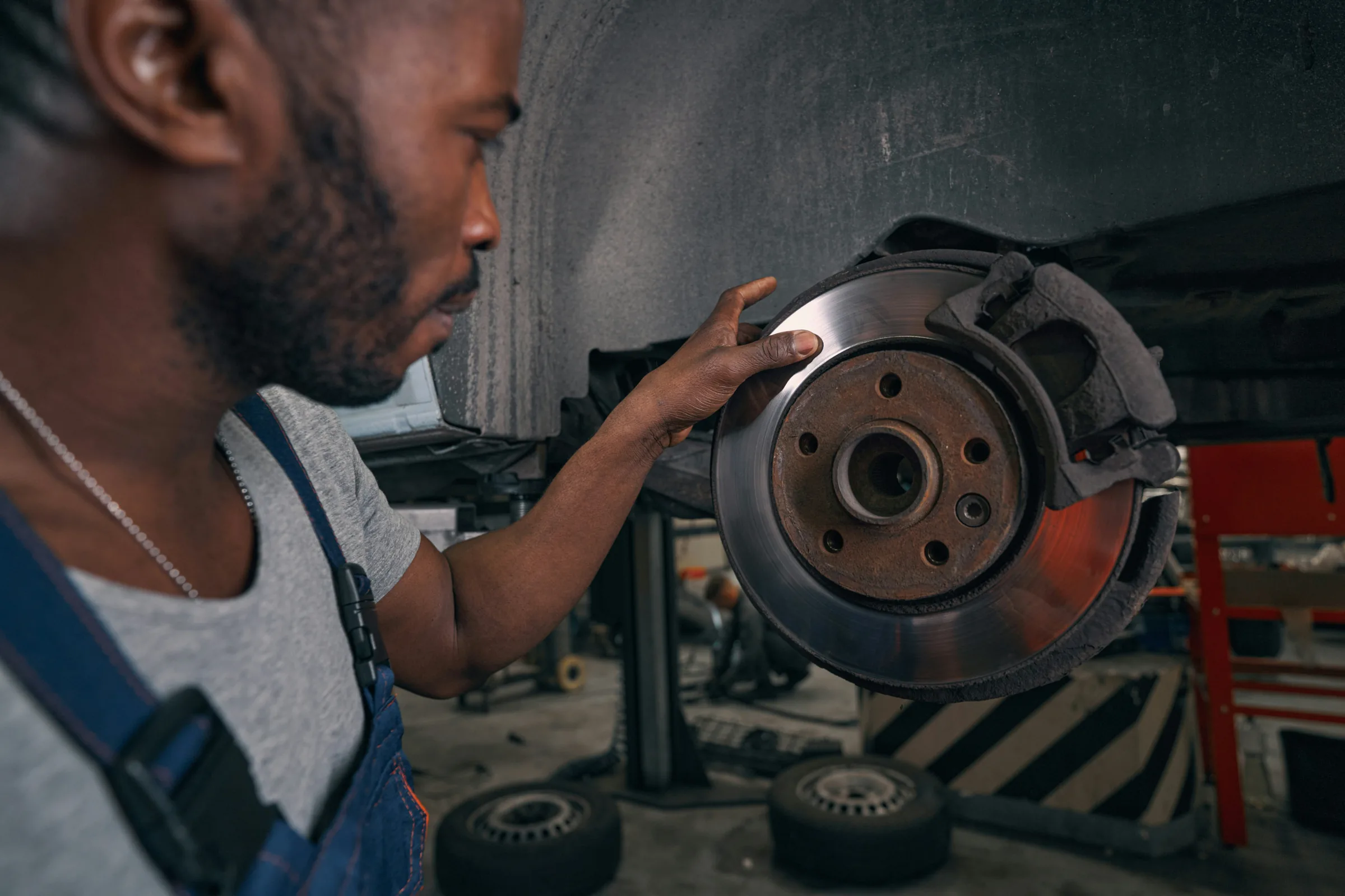 Technician examining a brake rotor and caliper by hand in a service bay. ABS Service in Kansas City, KS