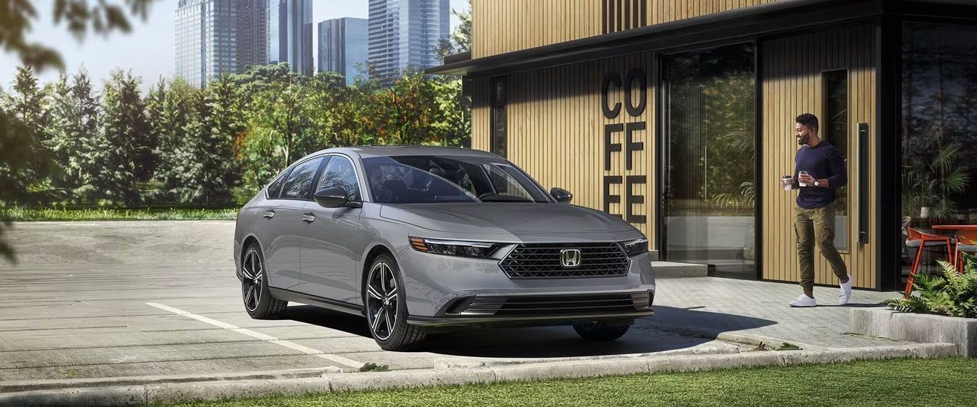 2024 Honda Accord Hybrid in a parking lot, in front of a coffee shop with a man holding two coffee cups.