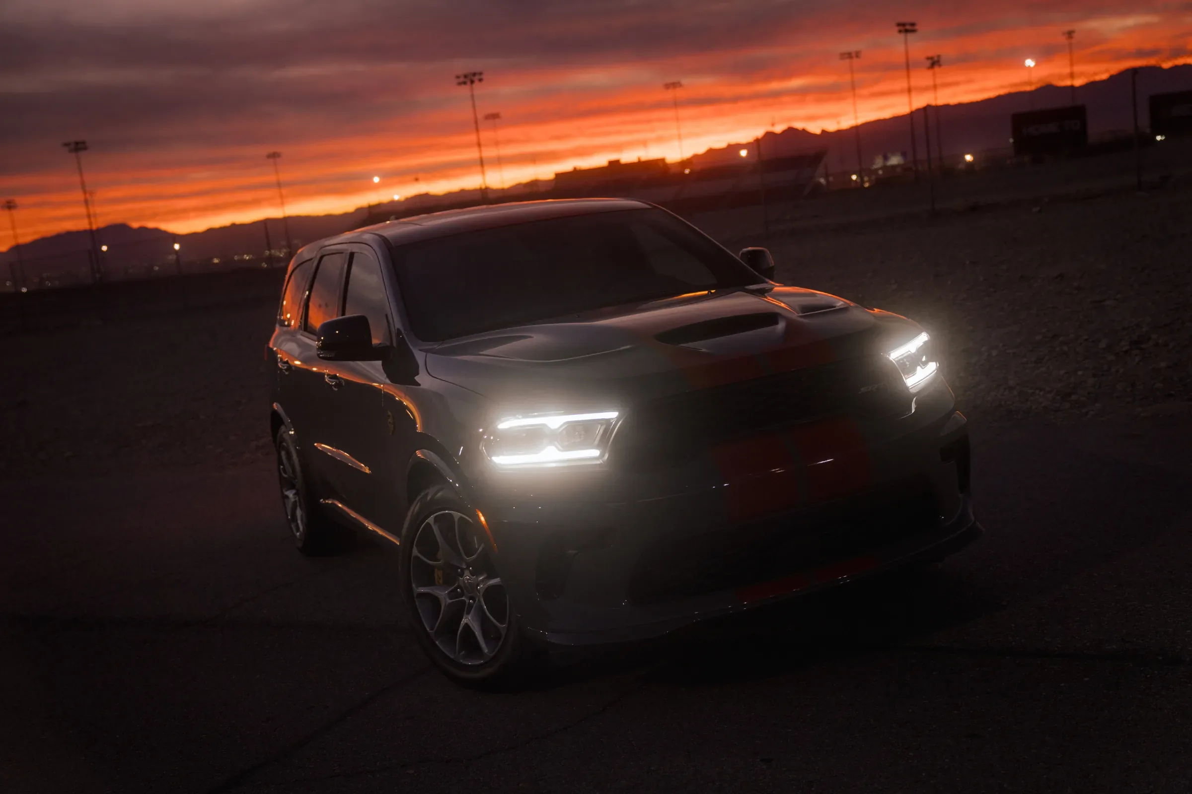 Dark-colored performance SUV with headlights on, parked on pavement at sunset with mountains in the background. Headlight Service Near Topeka, KS