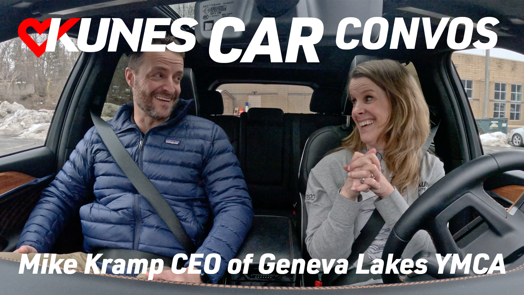 Text reads: Kunes Car Convos; Mike Kramp CEO of Geneva Lakes YMCA
Photo: Mike Kramp, CEO of Geneva Lakes YMCA, and Jen Myers, Marketing Director of Kunes Auto & RV Group, smile at each other while driving in a 2023 Grand Cherokee 4XE