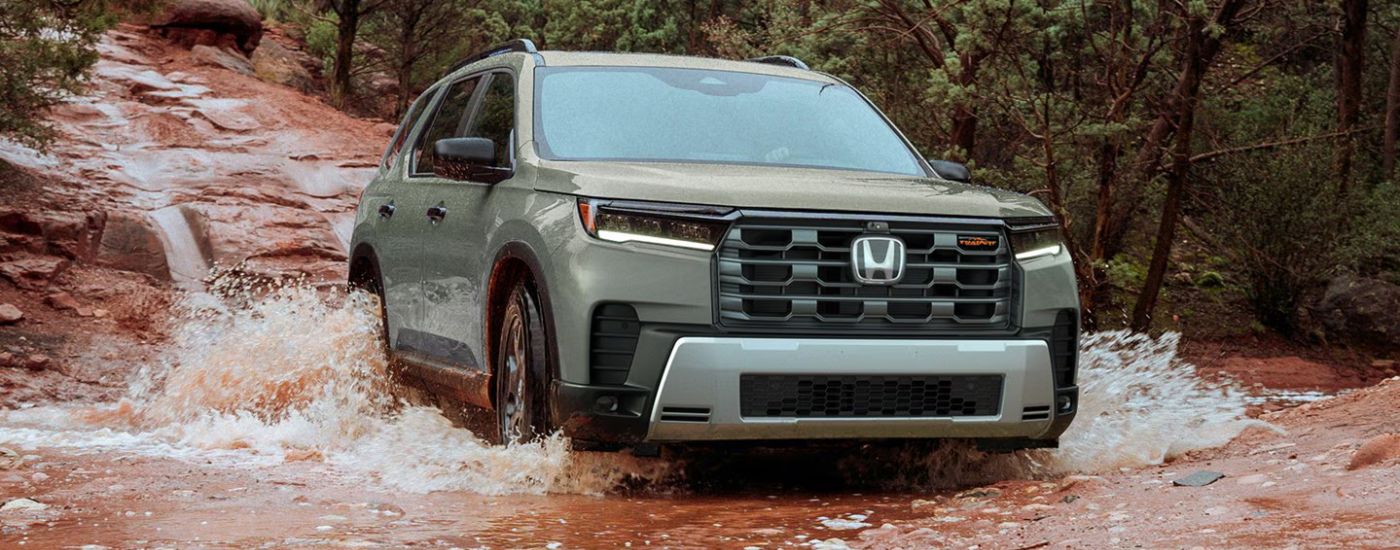 Green 2026 Honda Pilot Trailsport driving through a muddy river.