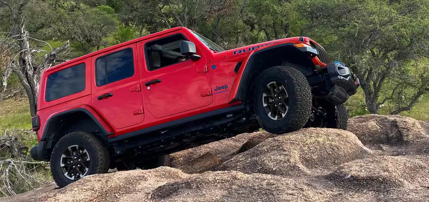 A red Jeep Wrangler sitting on to of rocks.