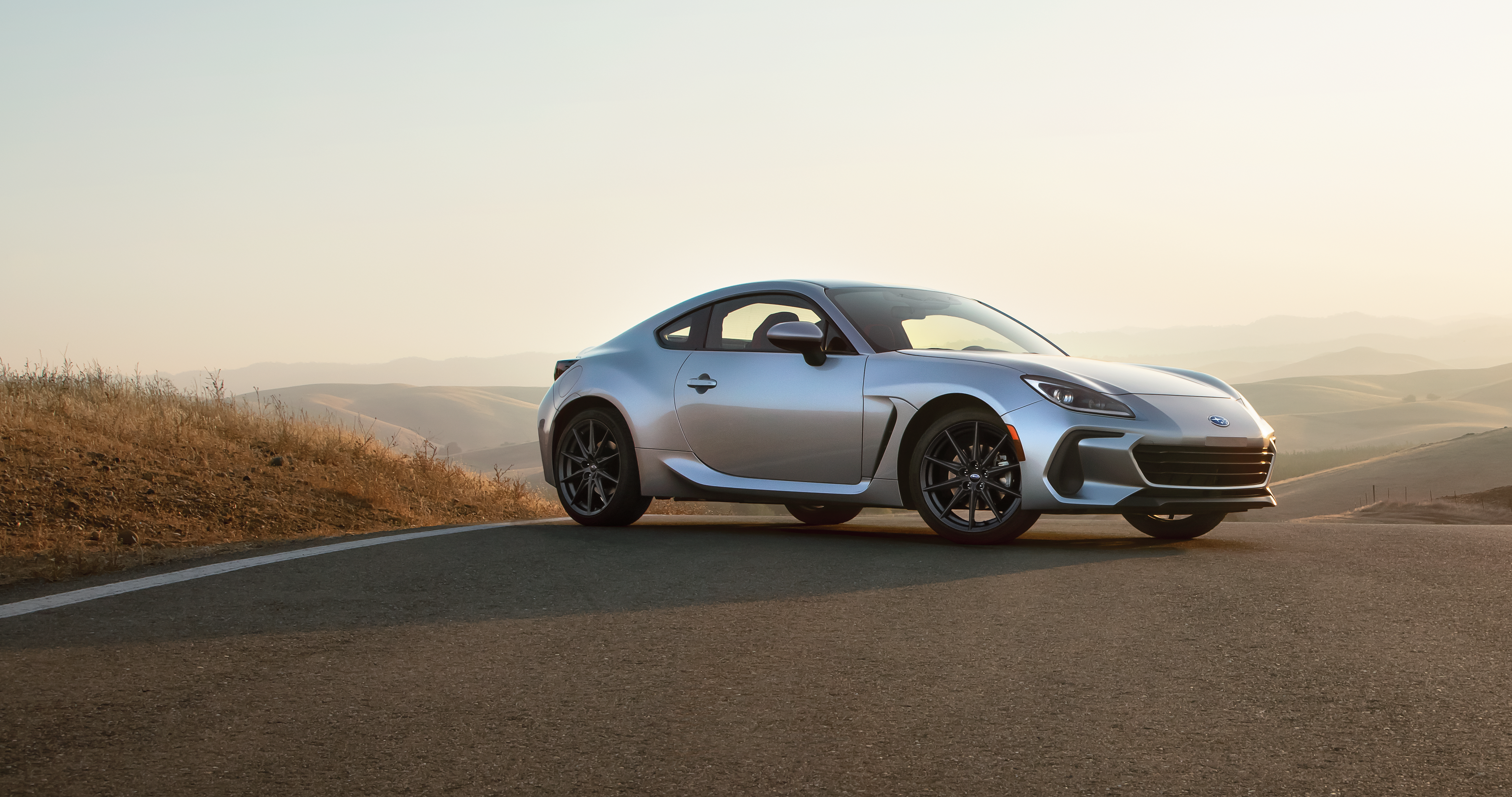 A silver BRZ parked on a road overlooking a hilly landscape.