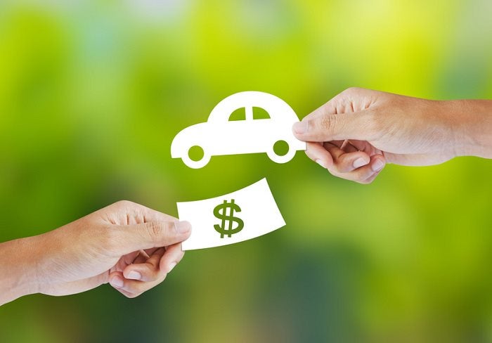 Hand offering a paper dollar sign in exchange for a paper car cutout, illustrating a car down payment