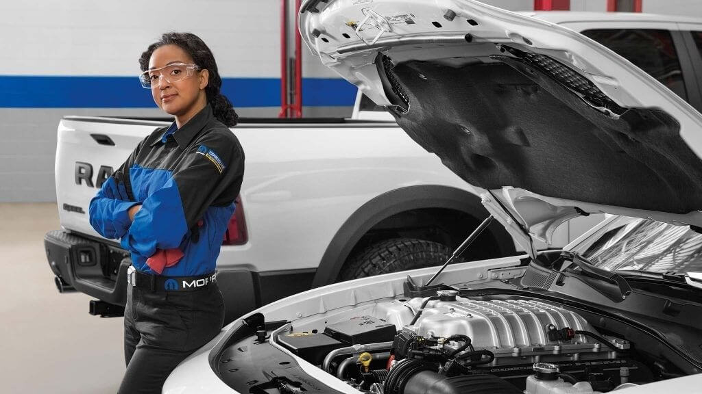 Mopar technician standing beside a white Ram truck with its hood open in the service bay