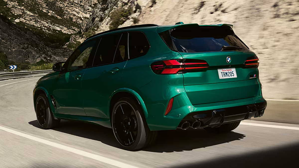 Rear view of a BMW SUV driving on a curved road surrounded by mountains