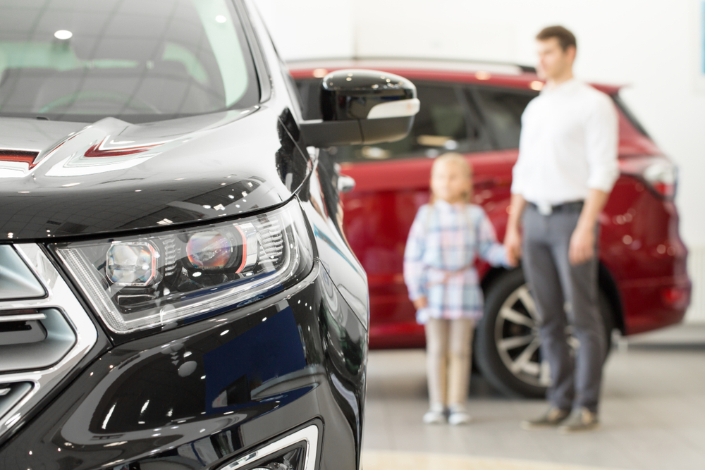 daughter and father in the background of photo, looking at vehicles in a dealership showroom