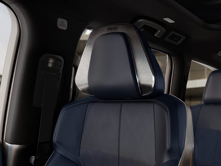 Close-up of a 2027 INFINITI QX80 front seat headrest with integrated Klipsch Reference Premiere speakers and navy perforated leather upholstery.
