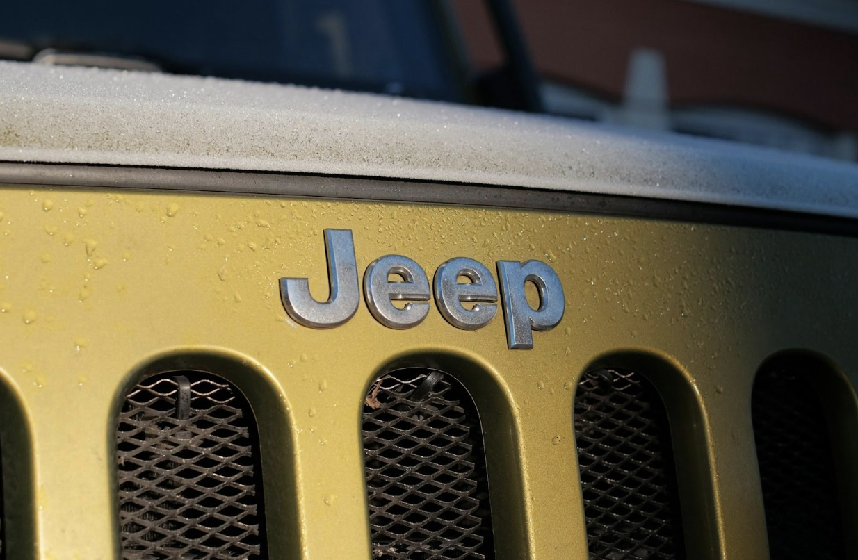 Close-up of the silver "Jeep" badge on the yellow grille of a vehicle, with frost on the hood.
