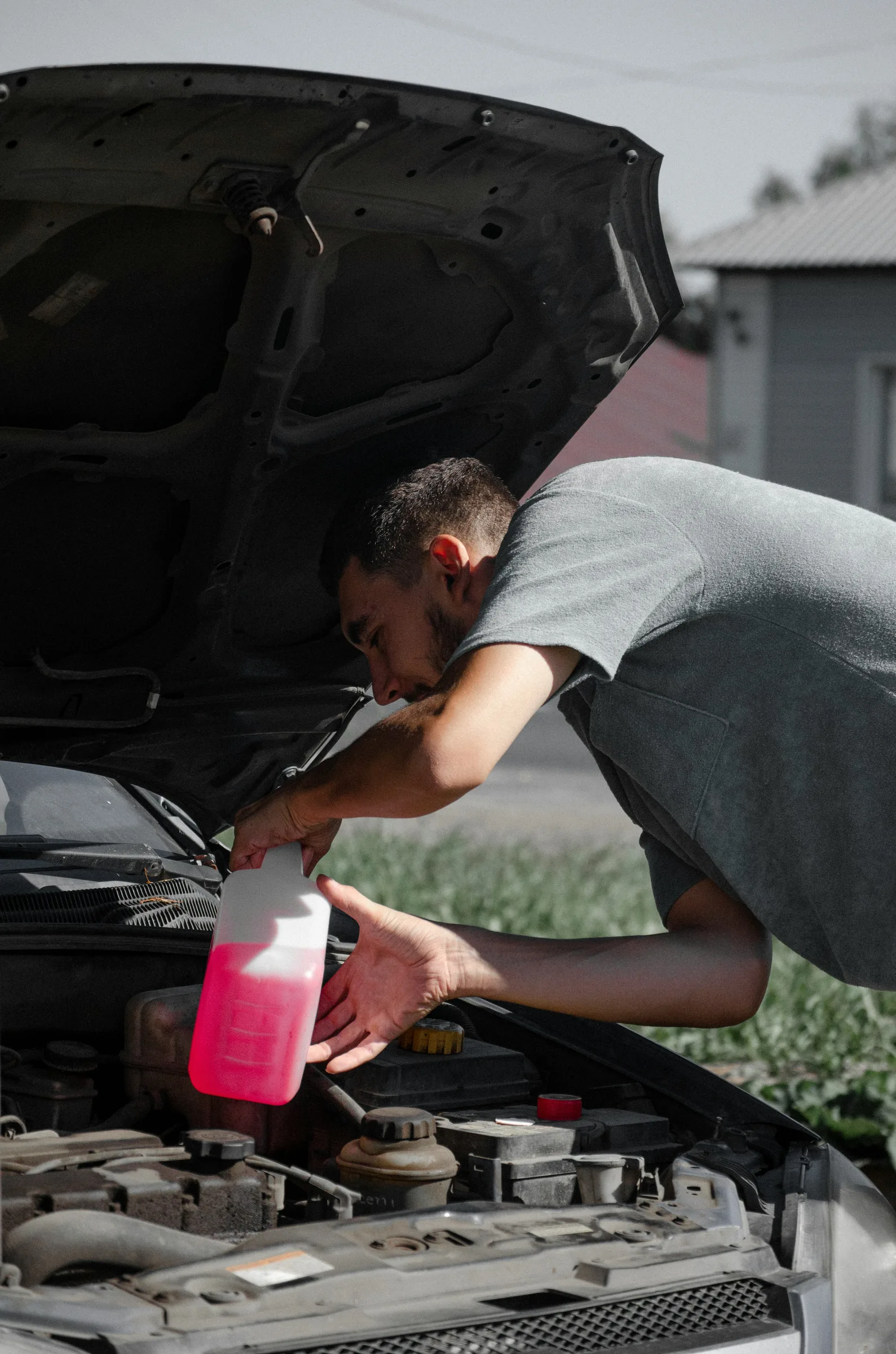 Technician leaning into an open engine bay while pouring pink coolant into the reservoir. Coolant System Service Near Kansas City
