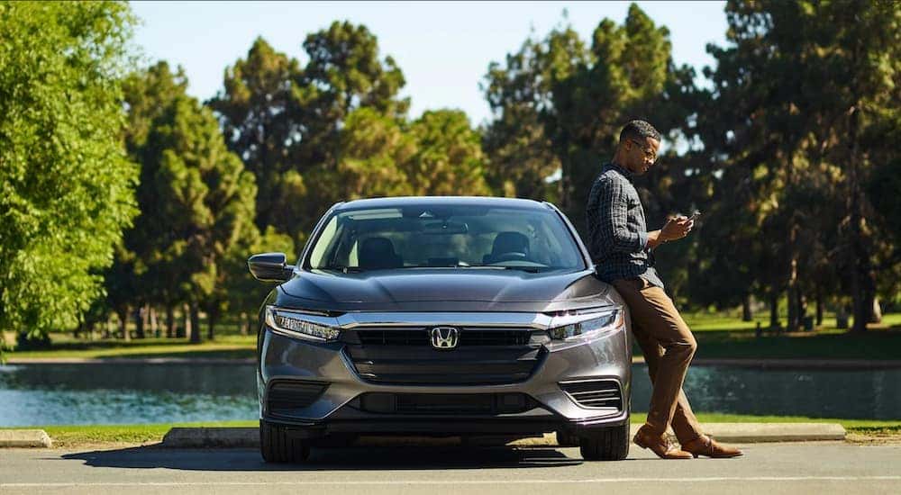 A person is shown leaning against a grey 2020 Honda Insight LX while looking at a smart phone