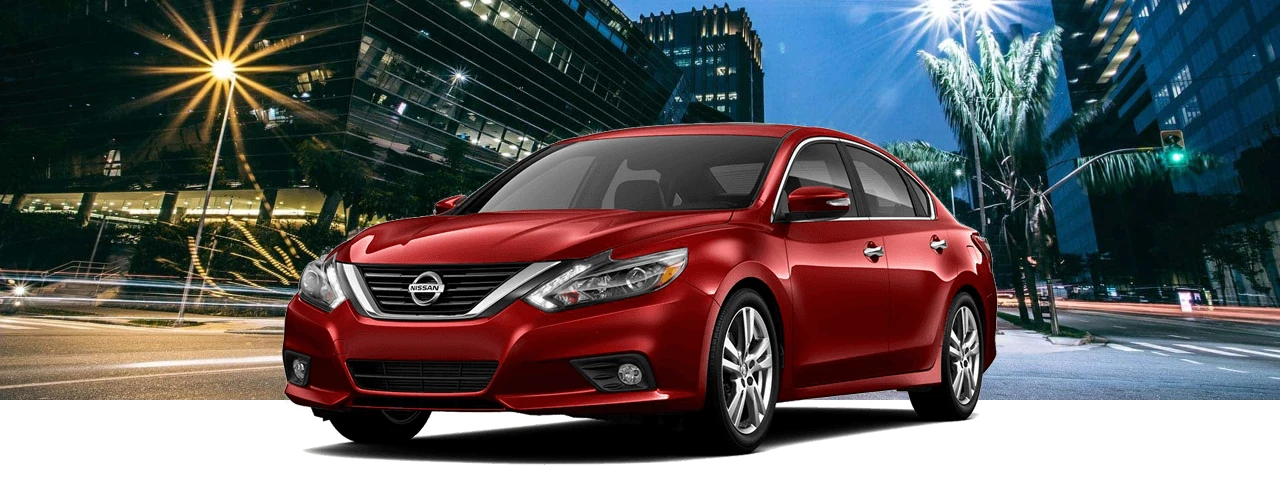 Red 2017 Nissan Altima sedan in front of a city street at night with glowing streetlights