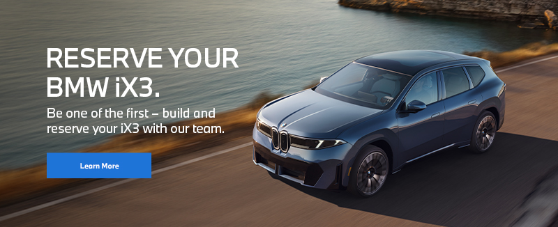 BMW iX3 vehicle driving on a road near mountains and water.