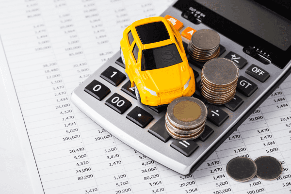 Toy car and stacks of coins on a calculator over financial spreadsheets